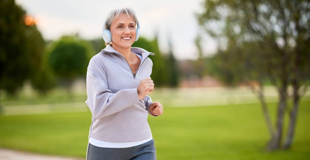 Older woman jogging and smiling, feeling more energizes and like herself after hormone therapy.