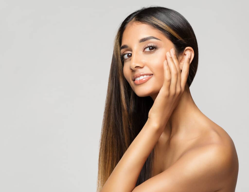 Beautiful young woman touching her face happily after getting under-eye filler for improved texture.