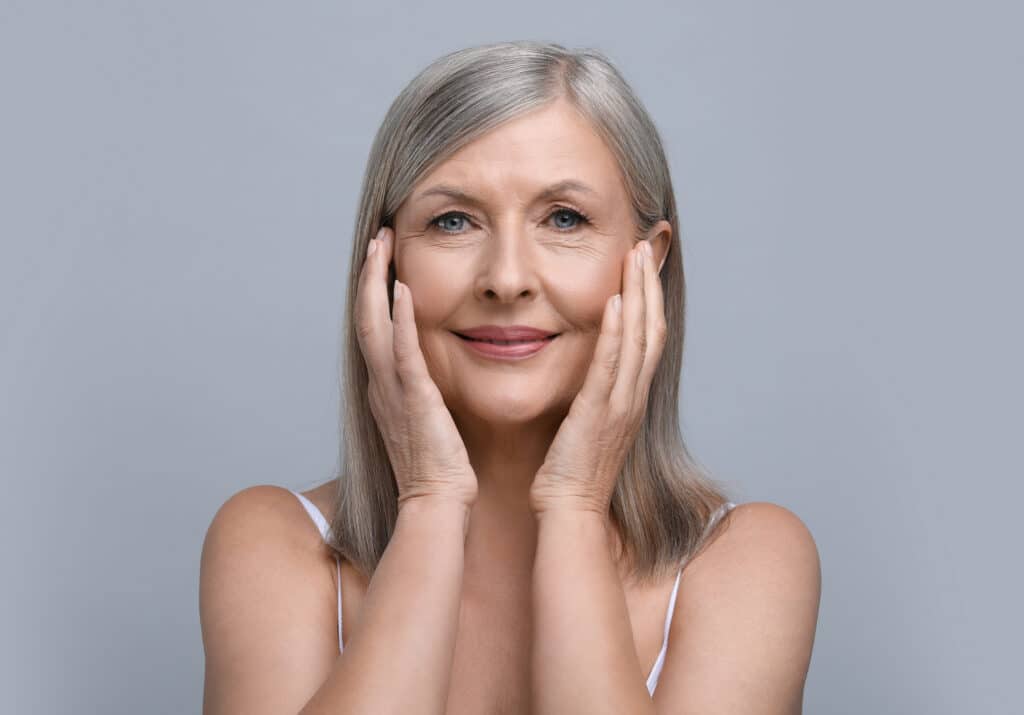 Older woman touching her face after getting Sculptra injections to improve facial volume loss.